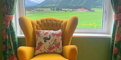 Gelber Ohrensessel vor einem Fenster mit Blick auf eine grüne Landschaft im Allgäu.
