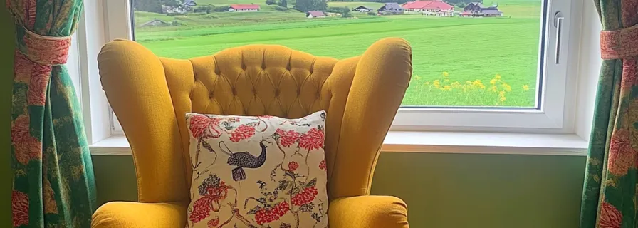Gelber Ohrensessel vor einem Fenster mit Blick auf eine grüne Landschaft im Allgäu.